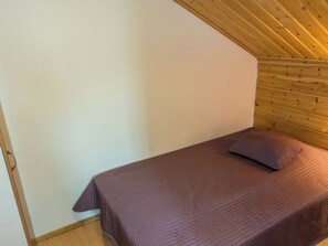 En enkel seng med gavl i et rum med skrå træloft og ensfarvede vægge.