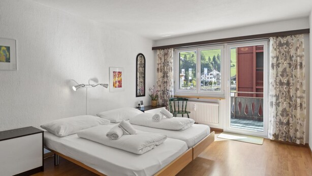 Ein modernes Schlafzimmer mit Bett, Nachttisch, Lampe und Fenster mit Vorhängen.