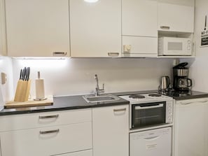 Cocina compacta con armarios blancos, un lavamanos, estufa, microondas y cafetera.