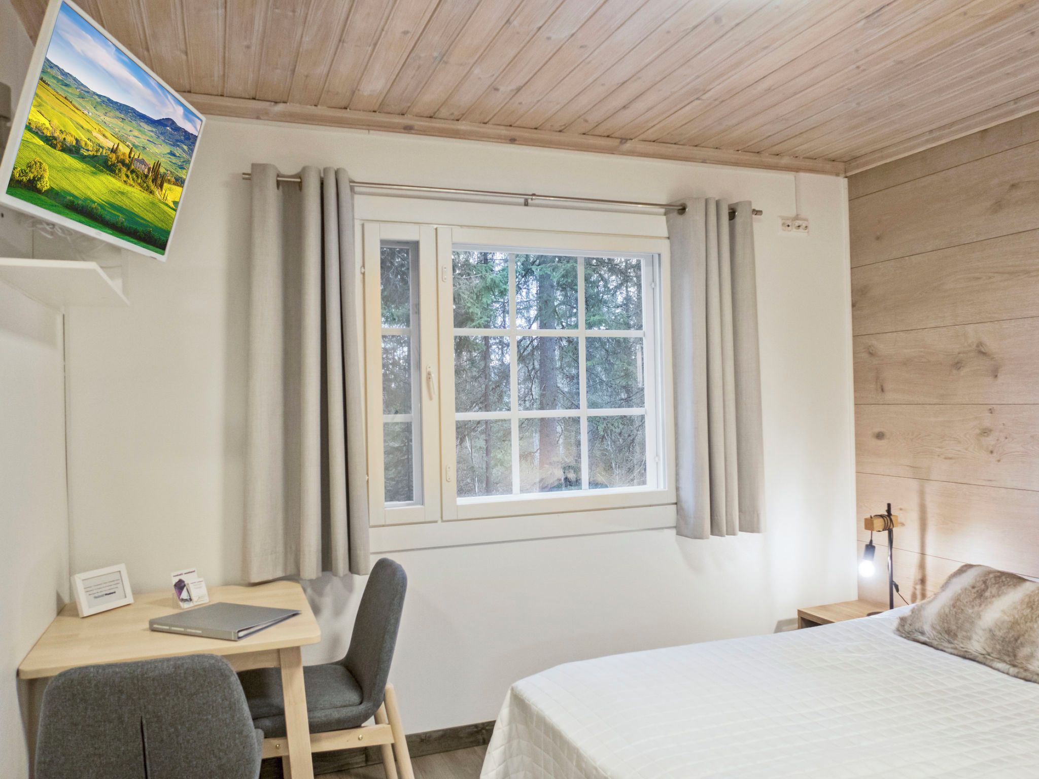 Una habitación con una cama, un escritorio con silla, un ventanal con cortinas e imagen colgada en la pared.