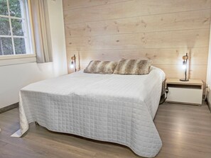 A neatly made bed with a quilted bedspread, two bedside lamps, and a wooden headboard. - Weekend duetto by Interhome (Sotkamo)