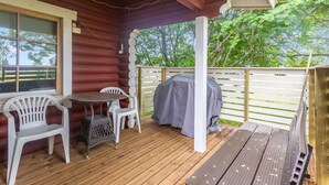 En overdækket træterrasse med et bord, stole, grill og udsigt til træer.