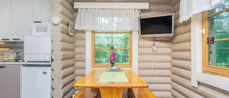 A log cabin interior with a wooden dining table, kitchen appliances, and a television.
