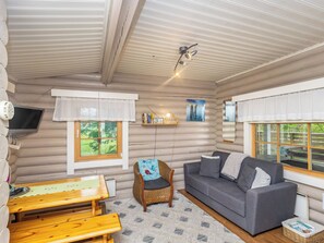 Ein rustikales Blockhaus-Interieur mit einer Couch, einem Sessel, einem Tisch und einem an der Wand befestigten Fernseher.
