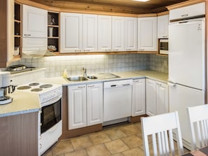 Una cocina moderna con muebles blancos, estufa, lavavajillas y refrigerador.