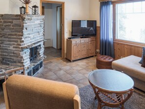 A living room with a stone fireplace, a television on a wooden cabinet, and a round table with chairs. - Rinnetupa by Interhome (Kuusamo)