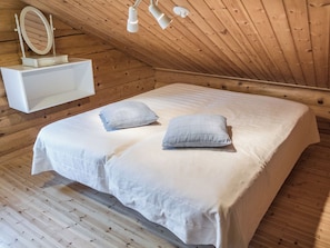 A bedroom with a wooden ceiling, a bed with white bedding, two pillows, a bedside table, and a mirror. - Rinnetupa by Interhome (Kuusamo)