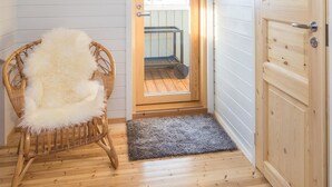 A wooden-framed door with a glass panel, a wicker chair with a fluffy white cushion, and a grey rug on a wooden floor. - Rinnetupa by Interhome (Kuusamo)