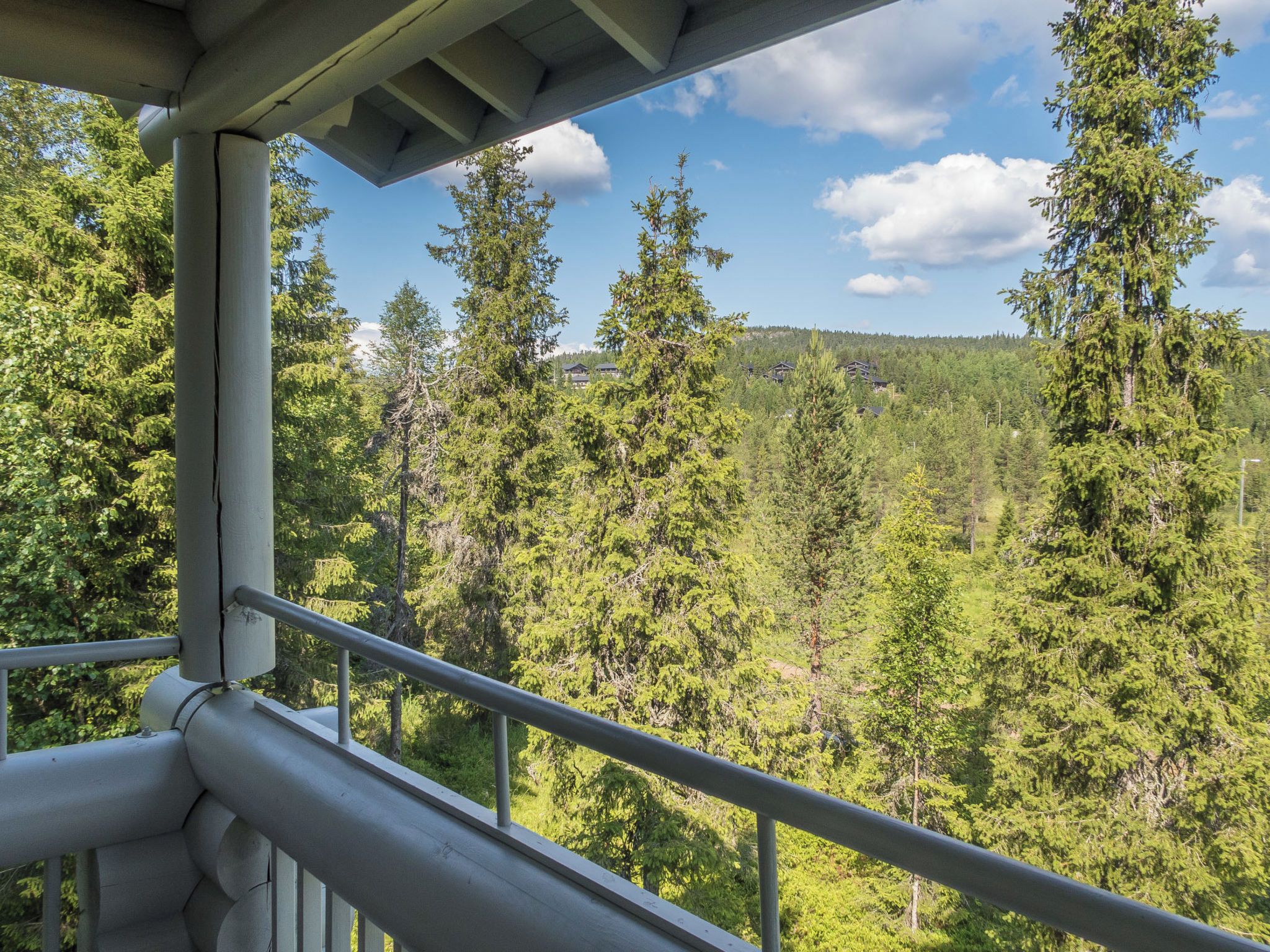 A balcony with a metal railing overlooking a forested area with tall trees and a clear sky.