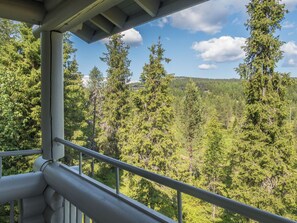 A balcony with a metal railing overlooking a forested area with tall trees and a clear sky. - Rinnetupa by Interhome (Kuusamo)