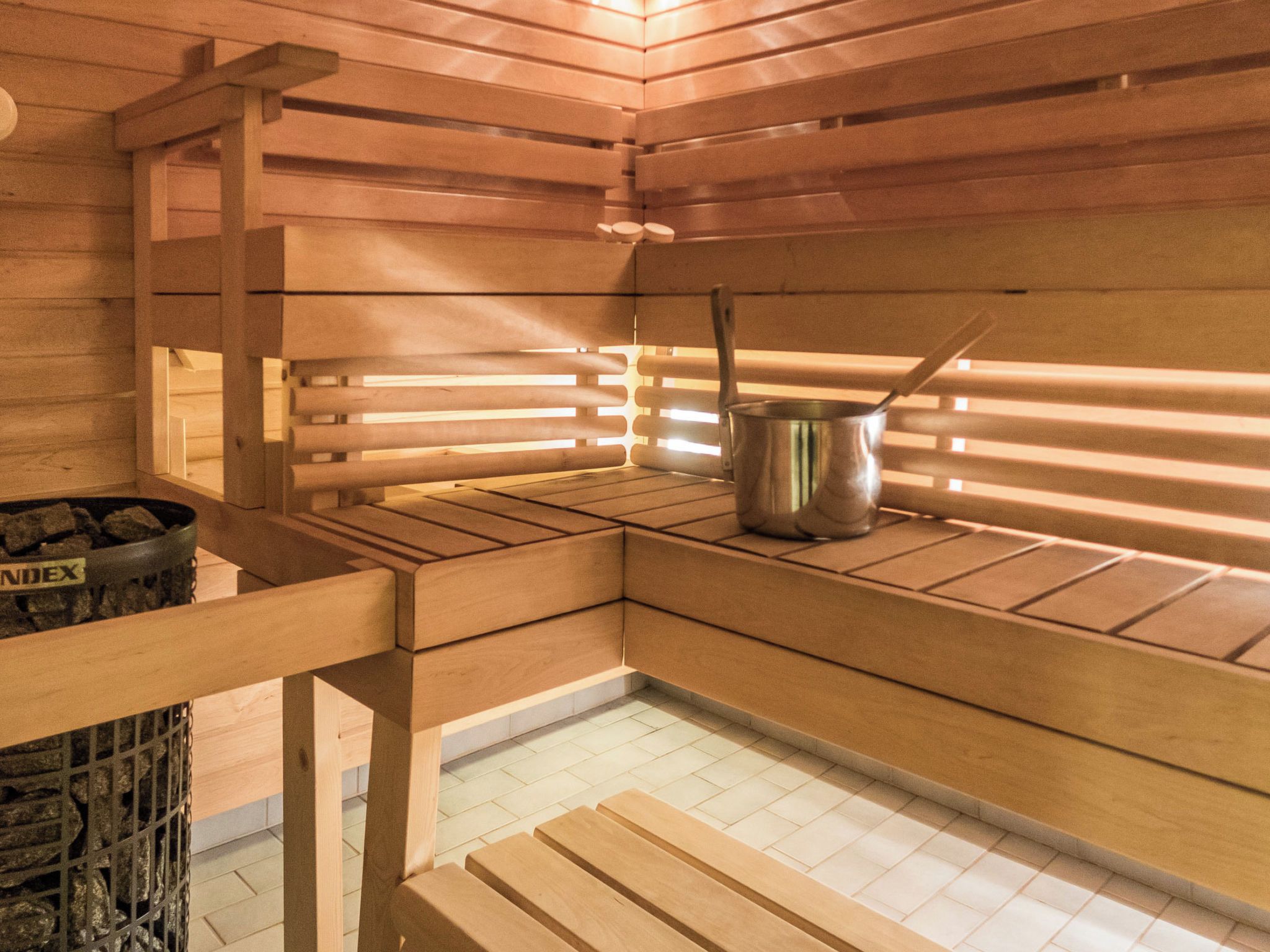 Eine Sauna mit Holzbänken, einem Metallbehälter und einem Steinkontainer mit der Aufschrift 'INDEX'.