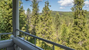 A view from a balcony with metal railings overlooking a forested area with tall trees and a distant hill. - Rinnetupa by Interhome (Kuusamo)