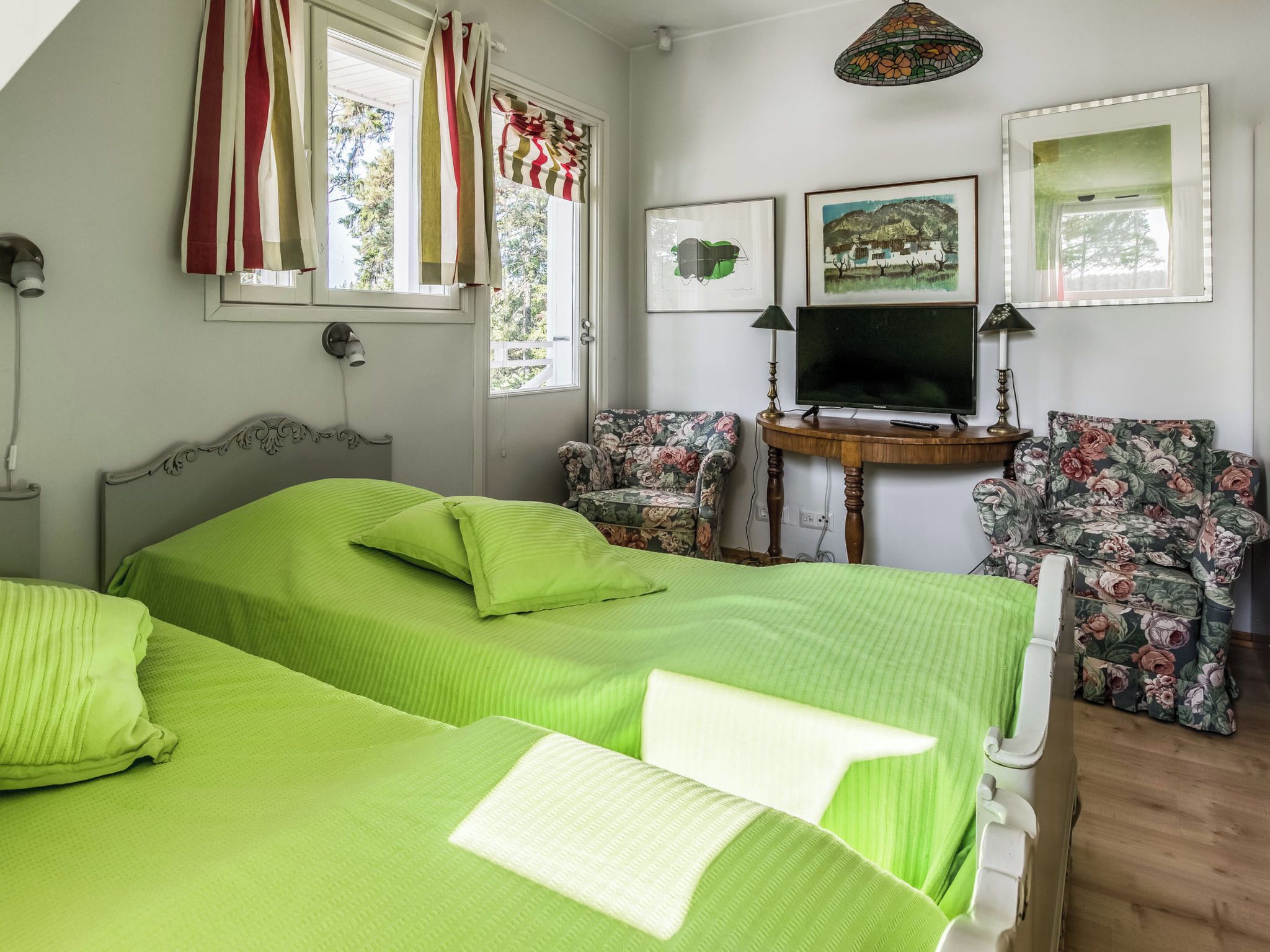 A bedroom with two beds, a television, and two chairs.