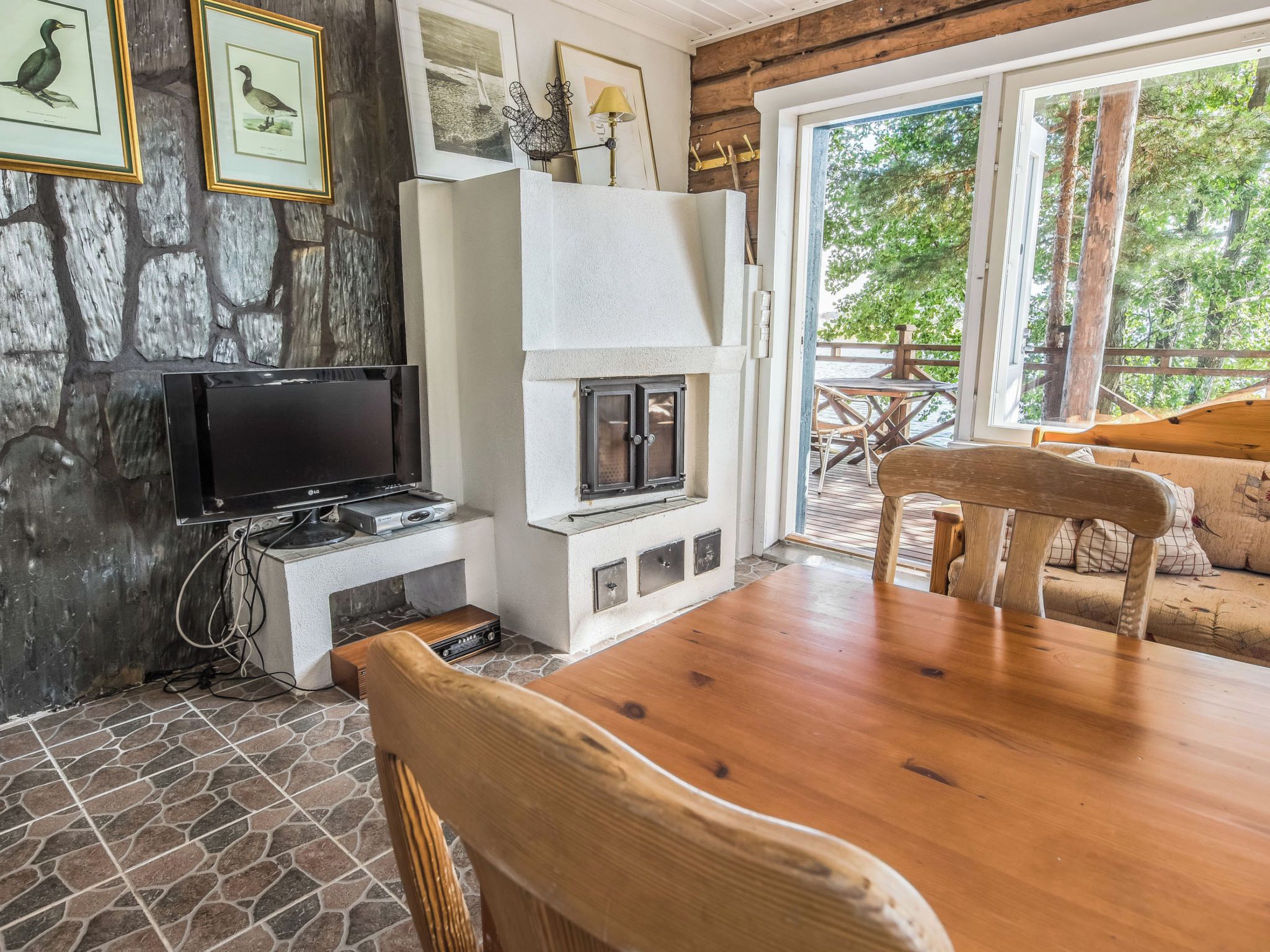 A cozy room with a stone wall, a fireplace, a television, and a wooden table with chairs.