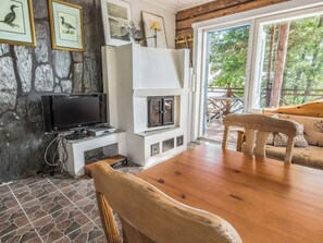 Une pièce chaleureuse avec un mur en pierre, une cheminée, un téléviseur et une table en bois entourée de chaises.