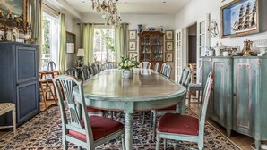 Ein Esszimmer mit einem großen runden Tisch, mehreren Stühlen, einer Chandelier und einem gemusterten Teppich.