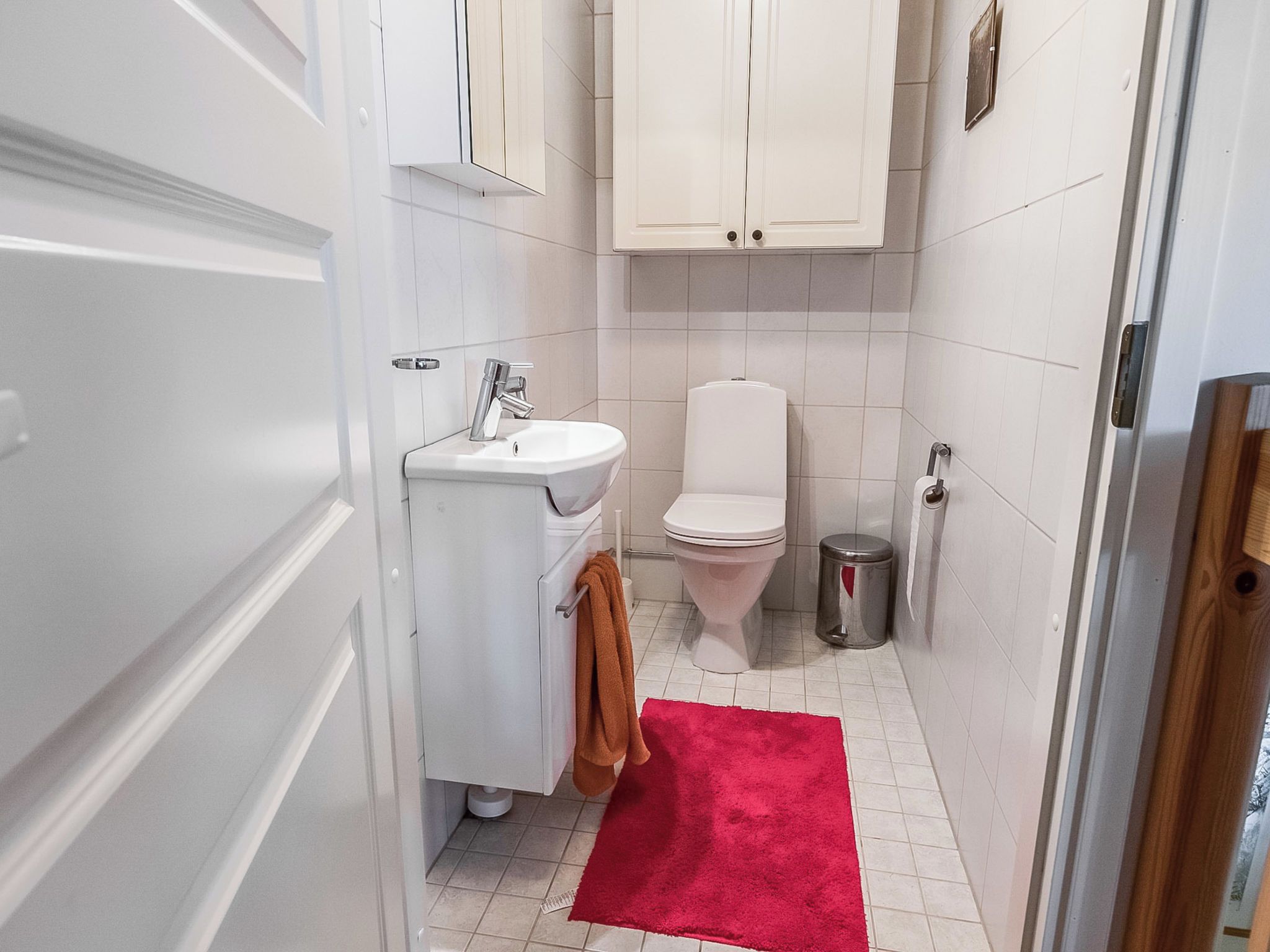 A bathroom with a white sink, toilet, and a red rug.