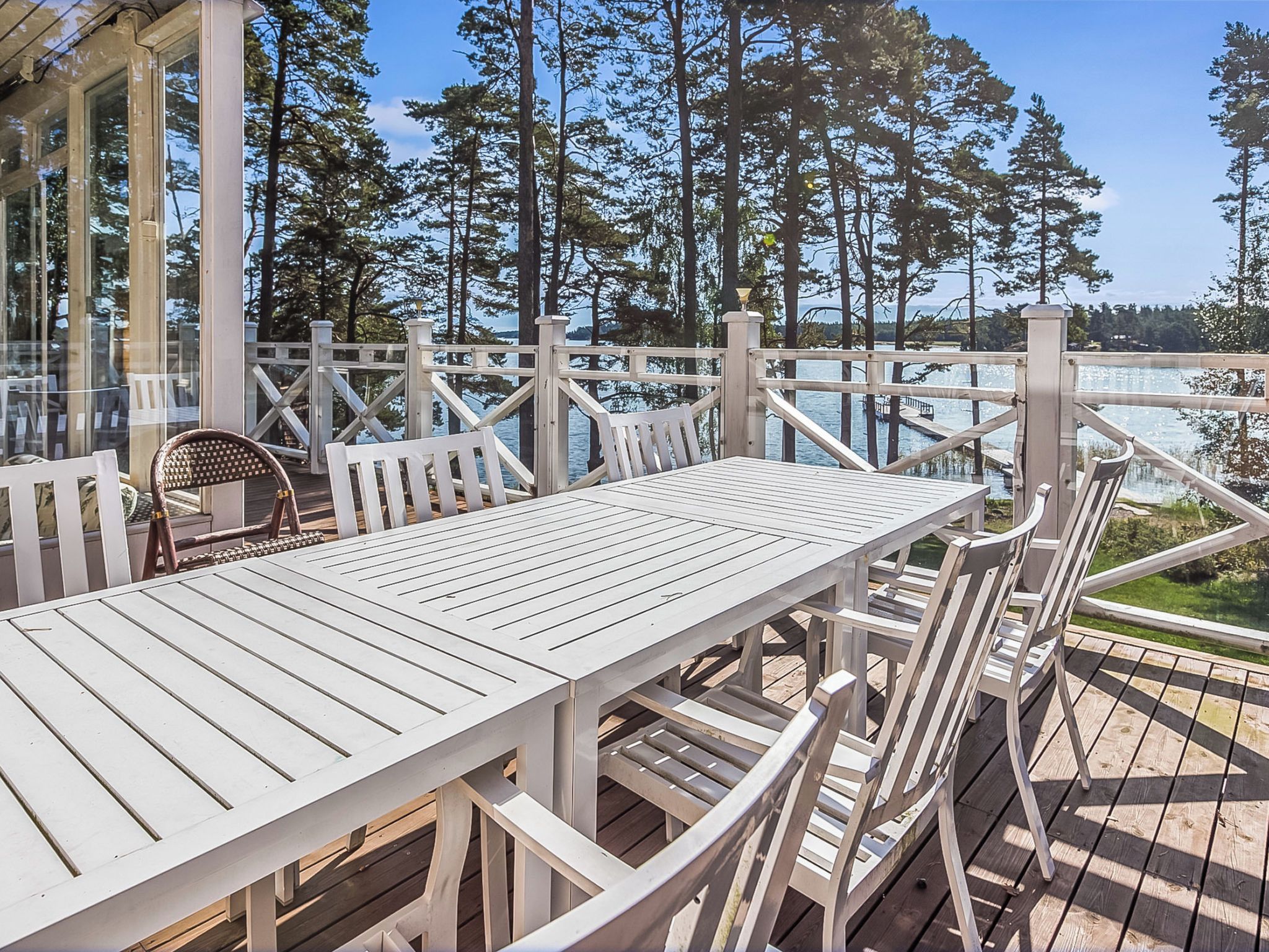 A wooden deck with a table and chairs, overlooking a body of water and surrounded by trees.