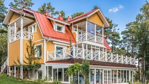 Ein zweistöckiges Haus mit rotem Dach, weißen Geländern und großen Fenstern.