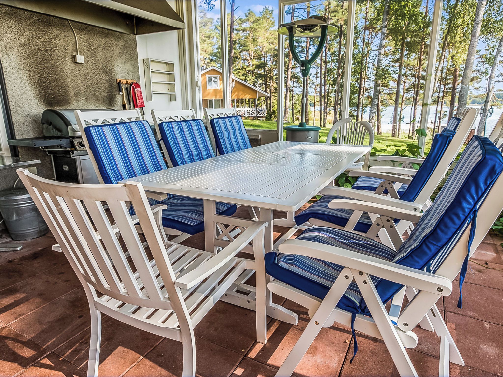 An outdoor patio with a table and chairs, a grill, and a view of a forest.