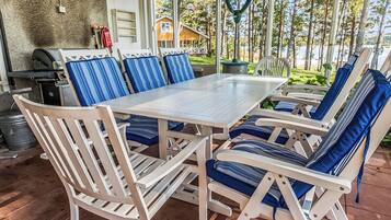 An outdoor patio with a table and chairs, a grill, and a view of a forest.