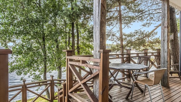 Eine Holzterrasse mit Tisch und Stühlen, mit Blick auf ein Gewässer.