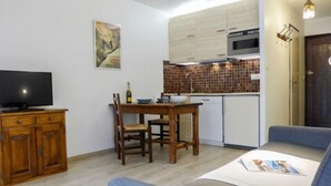 Un espace de vie compact comprenant une table à manger, un téléviseur posé sur un meuble en bois, une kitchenette équipée d’un four à micro-ondes et une porte avec un luminaire.