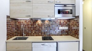 Une cuisine compacte dotée d’un four à micro-ondes encastré, d’un lave-vaisselle et d’un crédence carrelée.