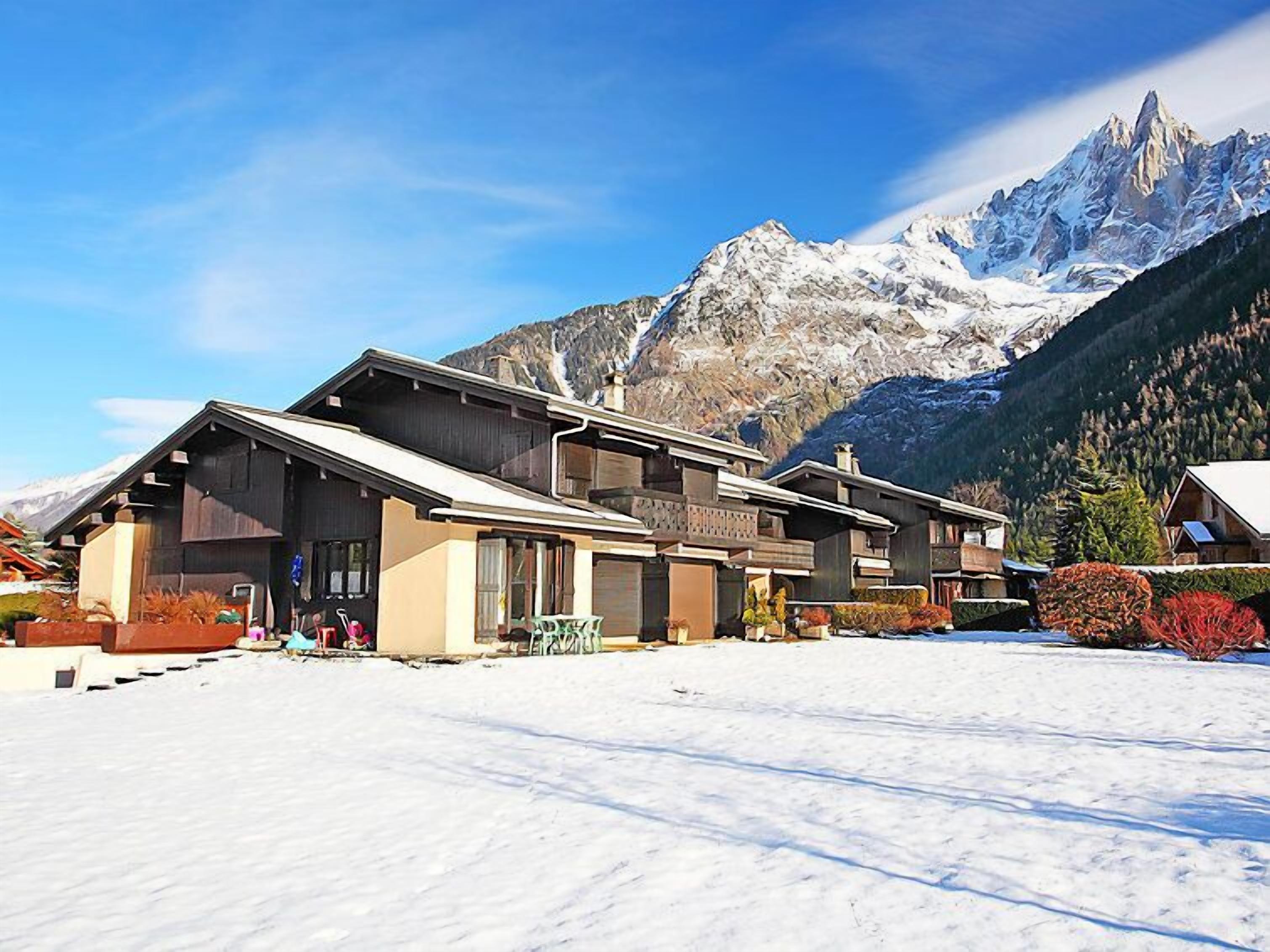 Ein Chalet mit geneigtem Dach, großen Fenstern und verschneitem Grund.