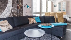 Een moderne woonkamer met een donkere bank, een ronde salontafel en een decoratieve schaal. Er is een kroonluchter, rieten meubels en een uitzicht op de stad door grote ramen.