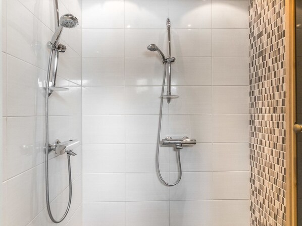 A bathroom with two showerheads, a handheld shower, and a tiled wall.
