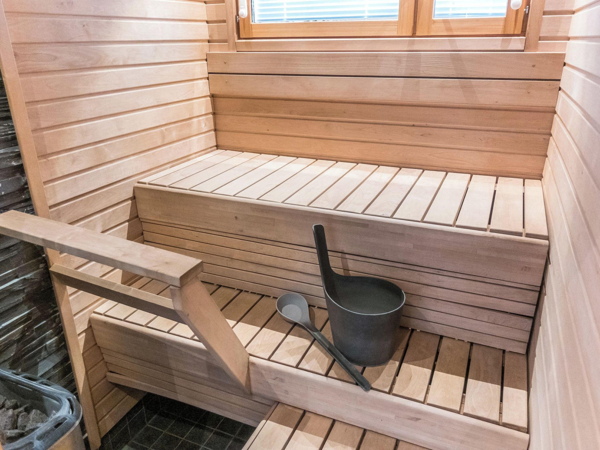 A sauna with wooden benches, a metal bucket, and a wooden ladder.
