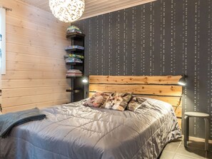 Ein Schlafzimmer mit einem hölzernen Kopfteil, einem Bett mit grauer Bettwäsche, einem kleinen runden Tisch und einem Regal mit Gesellschaftsspielen.