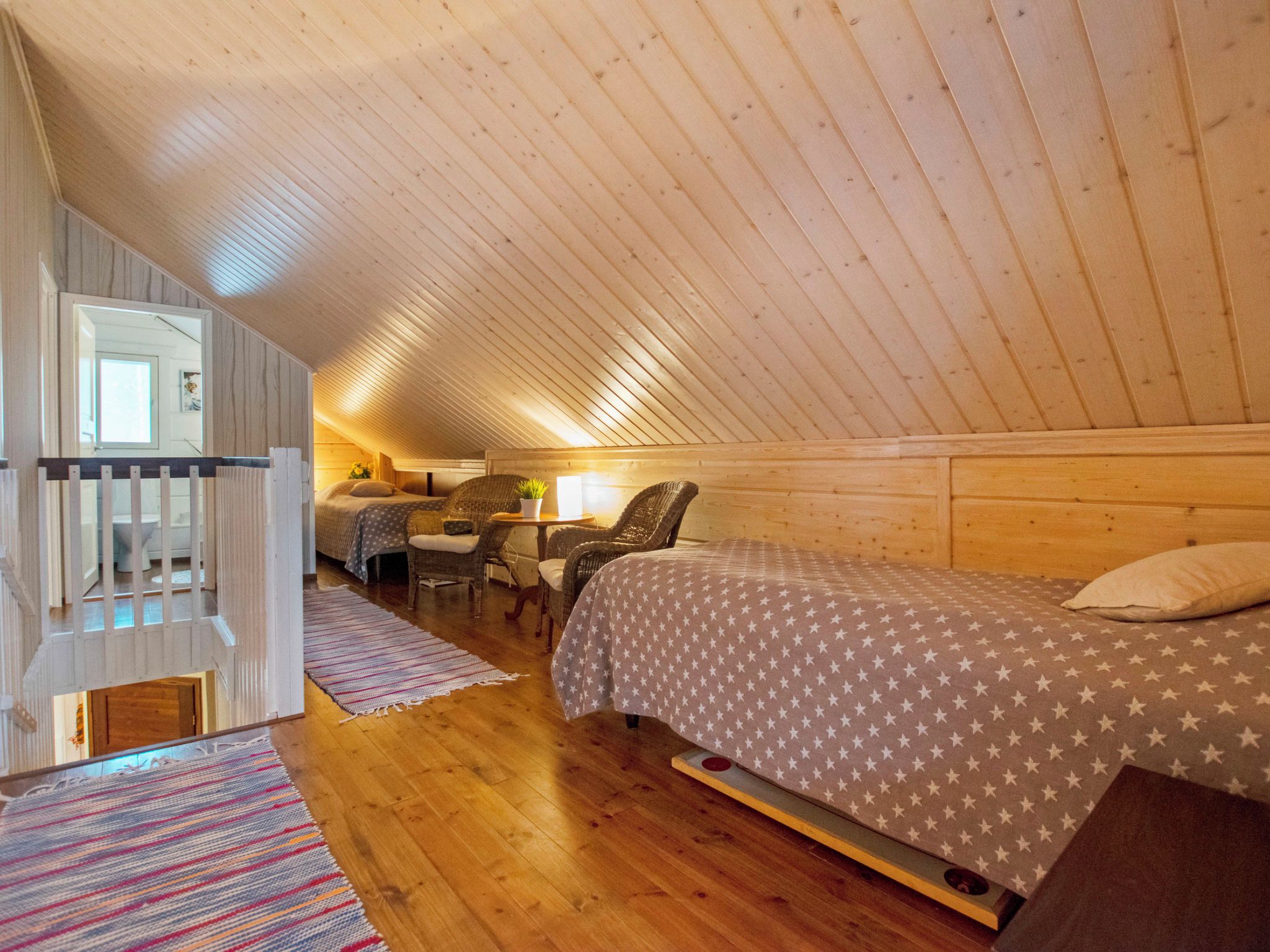 Un dormitorio acogedor en el ático con techo inclinado, una cama con colcha estampada de estrellas, un escritorio pequeño con silla y una alfombra colorida a rayas.