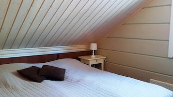 Et soveværelse med skråvæg, en seng med quiltet dyne, en sengetlampe og et vindue.