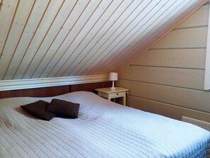A bedroom with a sloped ceiling, a bed with a quilted cover, a bedside lamp, and a window. - Loisteranta by Interhome (Ähtäri)
