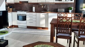 Een moderne keuken met witte kastjes, een fornuis en een vaatwasser. Er is een eethoek met houten stoelen en een tafel.