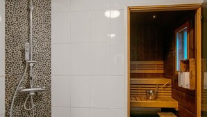 Een sauna met een stenen muur, houten banken en een douchegedeelte.