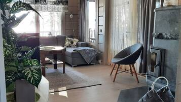 Moderni olohuone, jossa on sohva, nojatuoli ja sohvapöytä, suuri huonekasvi ja takka.