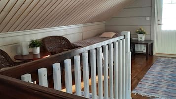A loft bedroom with a sloped ceiling, a wooden staircase, a cushioned seating area, a small table, and a potted plant.