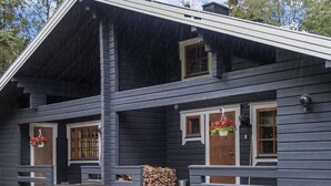 A two-story log cabin with a porch, wooden steps, and a stack of firewood.