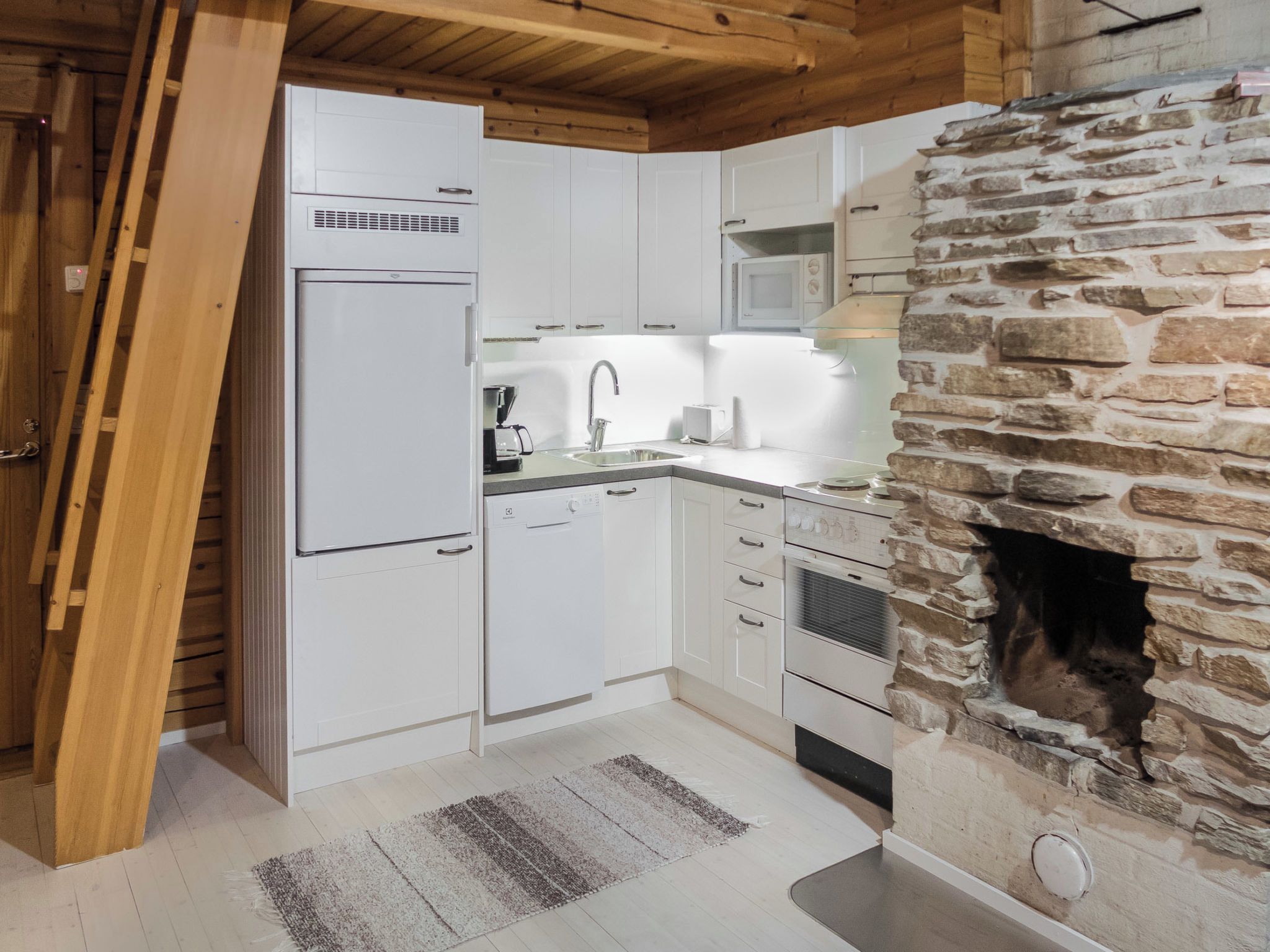 A kitchen with white cabinets, a stone fireplace, and a wooden ceiling.