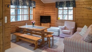 A cozy cabin interior with a wooden dining table, benches, a sofa, and a TV.