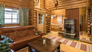A log cabin interior with a leather sofa, a wooden table, a fireplace, and a dining area. - Aurinkoniemi by Interhome (Hankasalmi)
