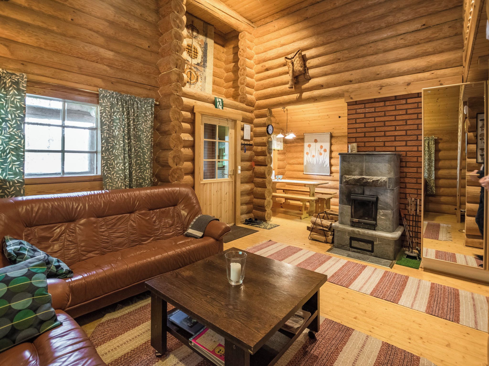 A log cabin interior with a leather sofa, a wooden table, a fireplace, and a mirror.