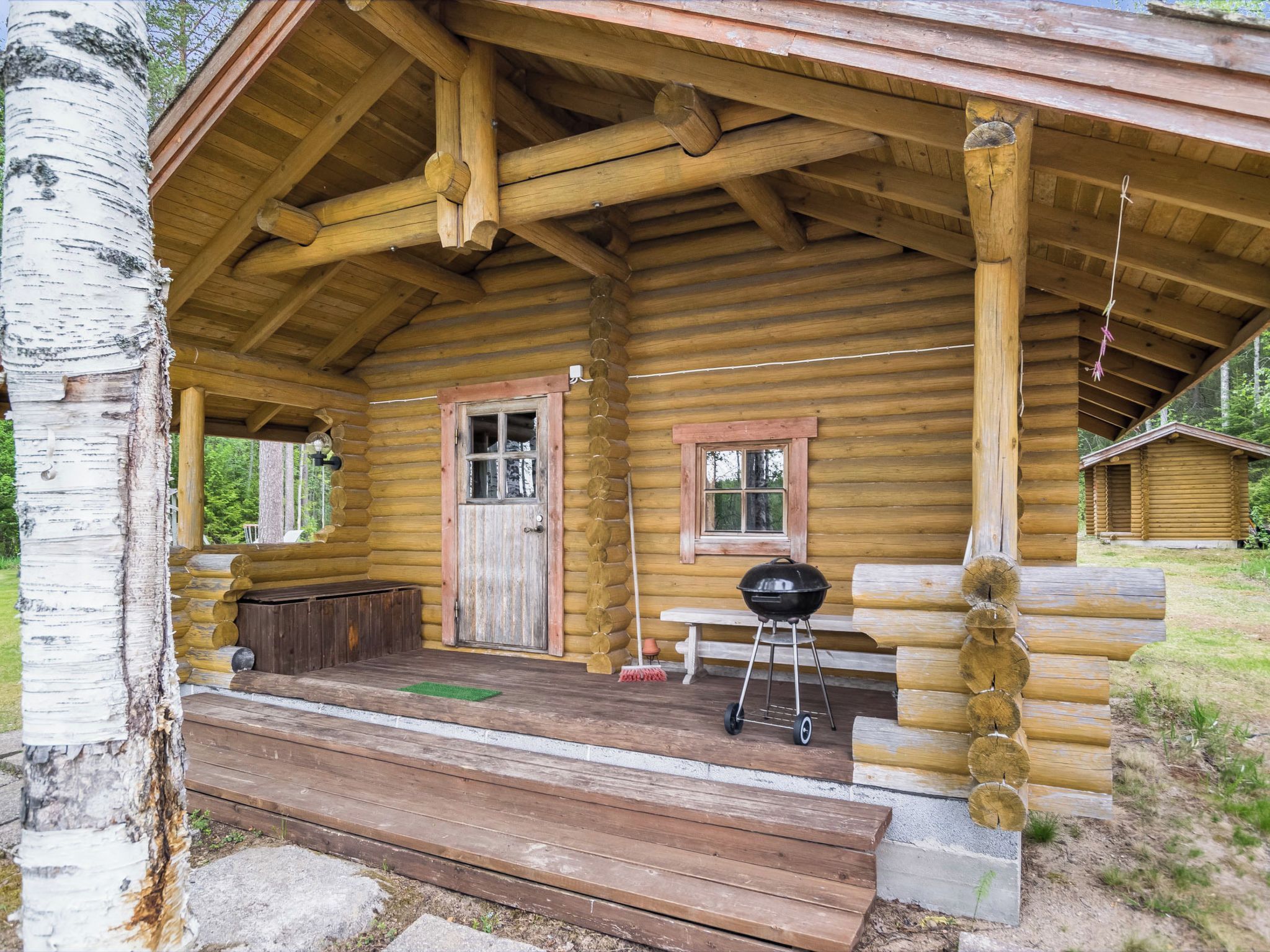 A log cabin with a porch, a door, a window, and a barbecue grill.