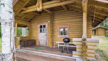 A log cabin with a porch, a door, a window, and a barbecue grill.