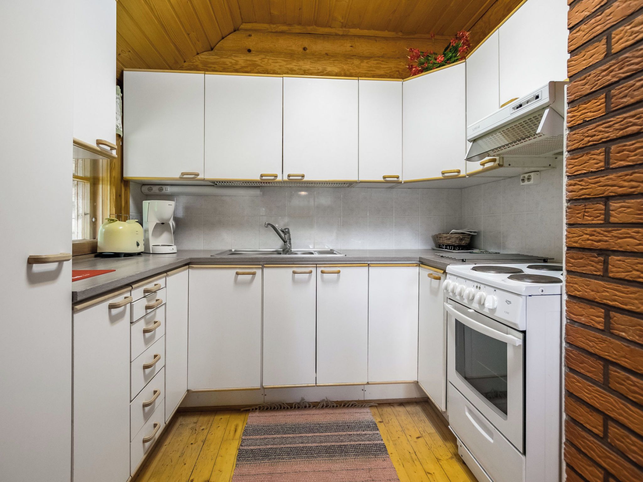 Una cocina compacta con armarios blancos, estufa integrada y cafetera.