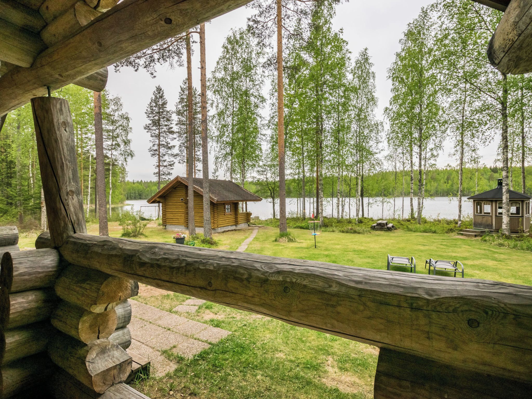Una cabaña con una terraza de madera que da a un lago, rodeada de altos árboles.