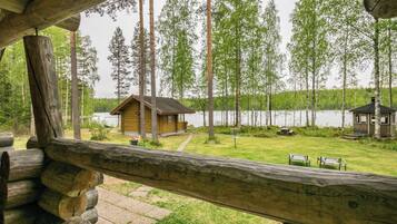 Una cabaña con una terraza de madera que da a un lago, rodeada de altos árboles.